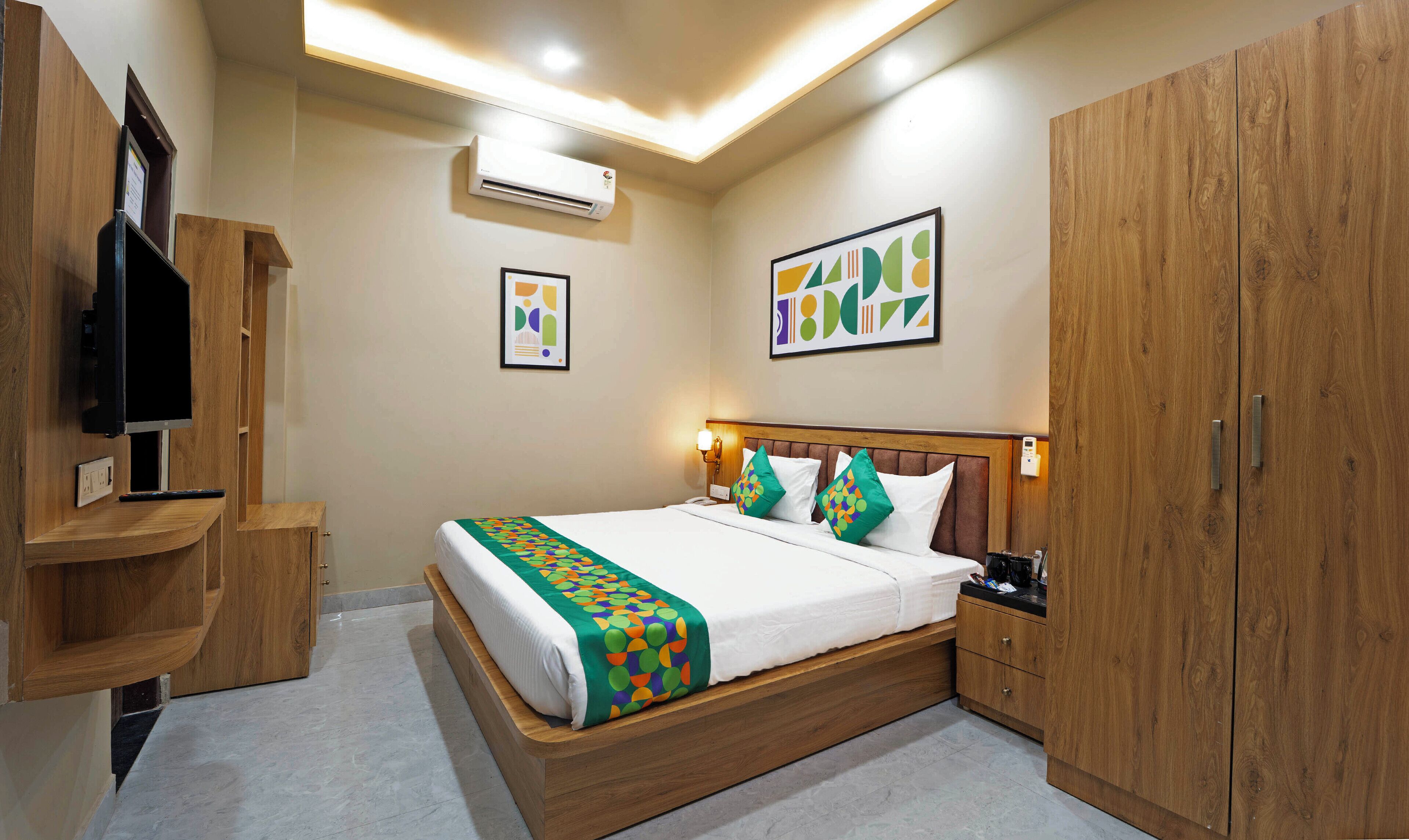 A hotel room with a wooden bed, a TV, a wardrobe, and artwork on the walls.