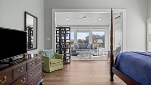 A bedroom with a large bed, a television, a dresser, and a seating area with a sofa and chairs.