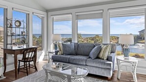 A spacious living room with a large window overlooking a scenic view, a comfortable sofa, a dining table, and a decorative metal shelf.