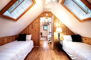 Een knus slaapkamer onder het dak met twee bedden, houten wanden en dakramen.