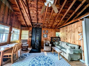 A wooden cabin interior with a fireplace, a sofa, a dining table, and a ceiling fan. - Gorgeous Waterfront Cabin for an Unforgettable Family Vacation by Georges Pond in Franklin, Maine (Franklin)