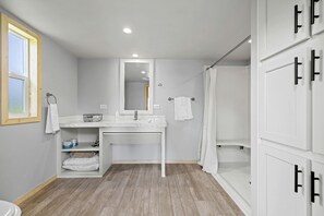 A bathroom with a white vanity, a mirror, a shower, and a wooden floor. - Glorious Cabin with Awesome Countryside Views in Fredericksburg, Texas (Fredericksburg)