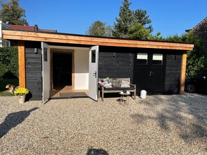 Een moderne houten chalet met een open deur, een bank met kussens en een kleine tafel met een theepot.