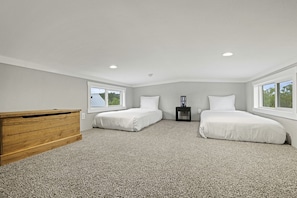Une chambre avec deux lits, une commode en bois, une table de chevet et une fenêtre.