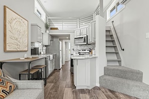Une cuisine compacte avec des meubles blancs, un coin repas doté d’une banquette et un escalier.