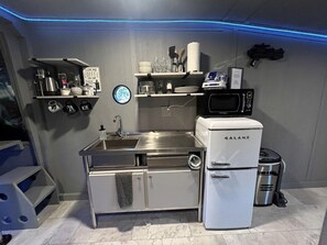 Eine kompakte Küche mit Spüle, einer Mikrowelle, einem Galanz-Kühlschrank und einer Ablage mit Küchenutensilien.
