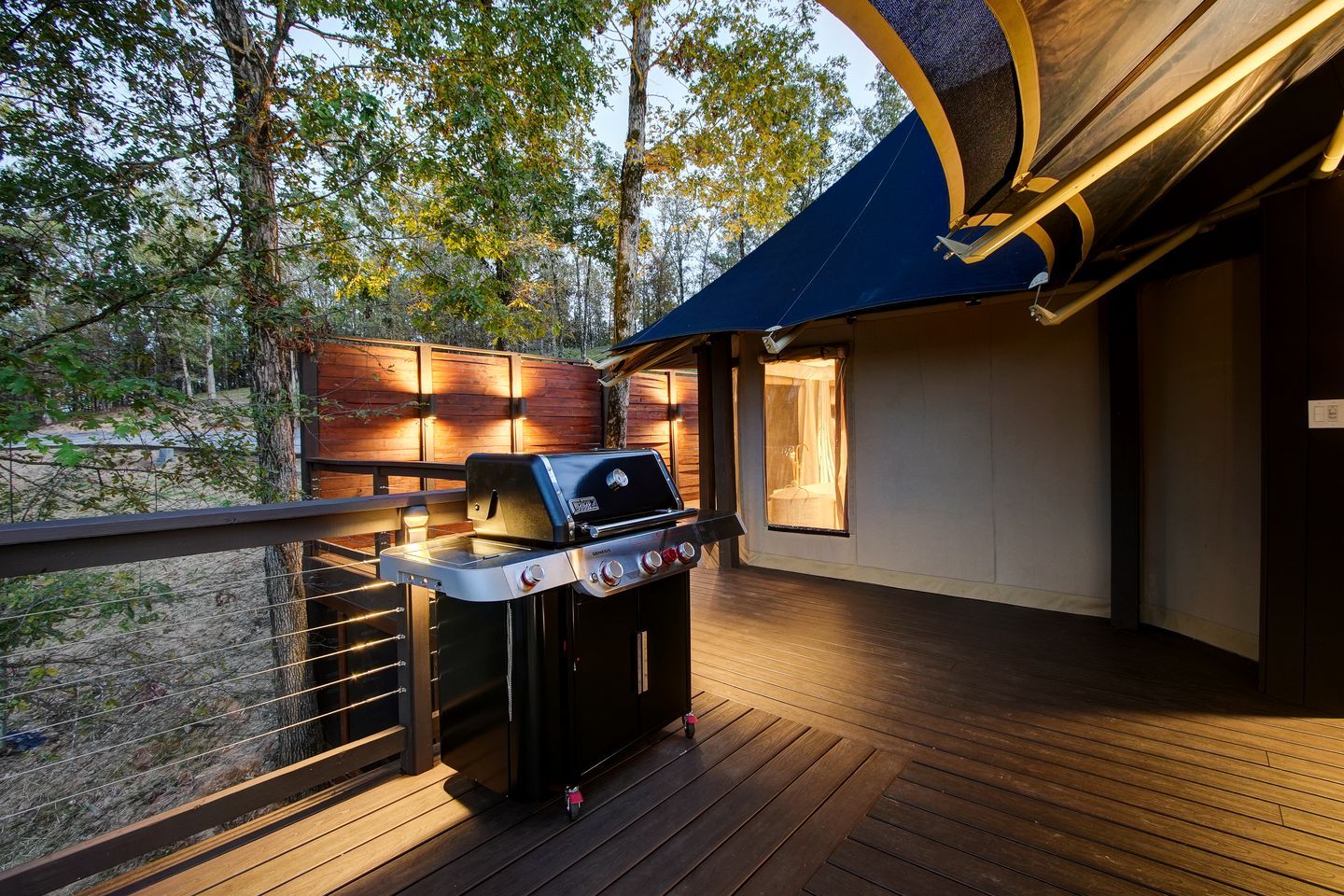 Ein überdachter Außenbereich mit Grill, einer Holzterrasse und Blick auf den umliegenden Wald.