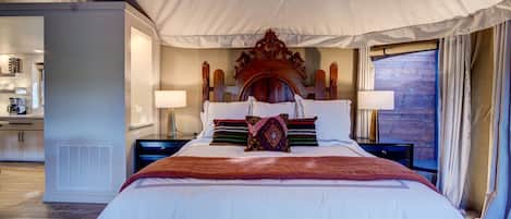 A spacious bedroom with a large bed, a wooden headboard, bedside lamps, and a view of a wooden deck.