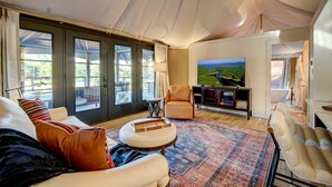 Un salón comedor amplio con un televisor grande, asientos cómodos y vistas a un lago a través de ventanas amplias.