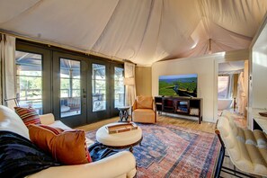 A spacious living room with a large TV, comfortable seating, and a view of a lake through large windows.