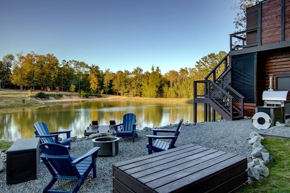Une terrasse au bord du lac, avec des fauteuils Adirondack, un foyer et un barbecue.