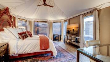 A bedroom with a large bed, a ceiling fan, a TV, a small table, and a chair.