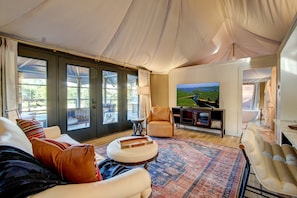 Ein geräumiges Wohnzimmer mit großem Fernseher, bequemen Sitzmöglichkeiten und Seeblick durch große Fenster.