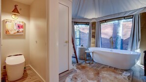 Une salle de bain avec une baignoire, un plancher en bois, un tapis et un tableau au mur.