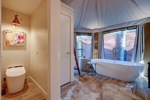A bathroom with a bathtub, wooden flooring, a rug, and a painting on the wall.
