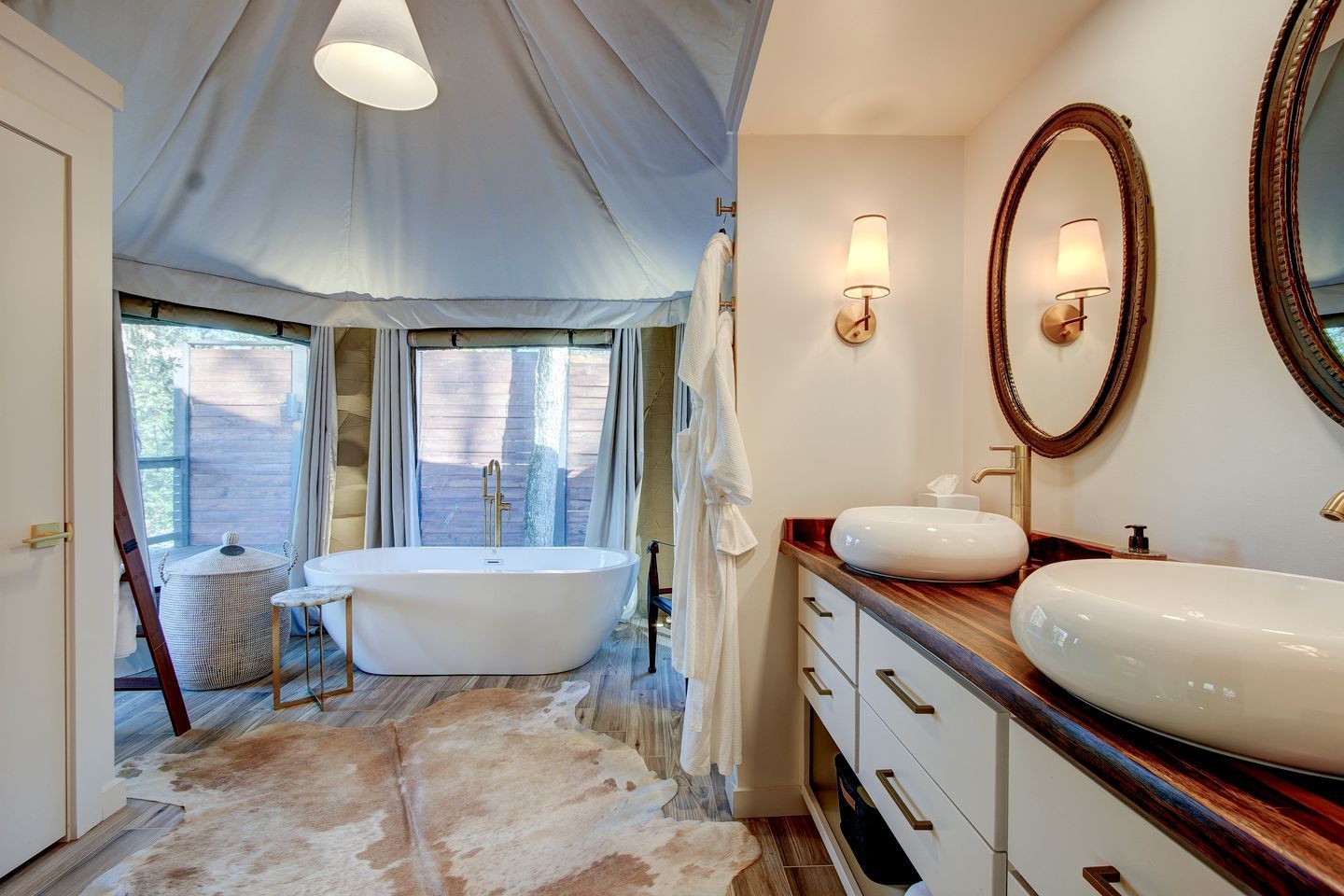 A bathroom with a freestanding bathtub, a vanity with a large mirror, and a window with curtains.