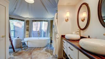 A bathroom with a freestanding bathtub, a vanity with a large mirror, and a window with curtains.