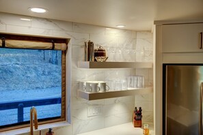 A modern kitchen with marble countertops, a built-in wine cooler, and a stainless steel refrigerator.
