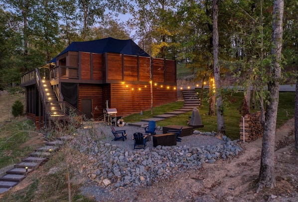 A wooden cabin with a deck, outdoor seating, and a barbecue area.