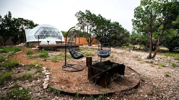 A modern outdoor seating area with two black chairs, a small fire pit, and a transparent dome structure in the background.