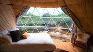 Une chambre avec une grande fenêtre, un lit, une chaise et une vue sur la verdure environnante.