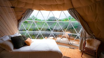A bedroom with a large window, a bed, a chair, and a view of greenery outside.