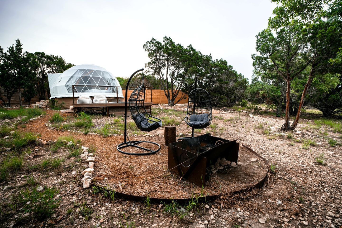 A modern outdoor seating area with two black chairs, a small fire pit, and a transparent dome structure in the background.