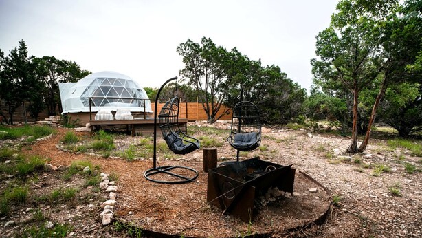 Un espace extérieur moderne aménagé avec deux chaises noires, un petit foyer et, au fond, une structure en forme de dôme transparent.