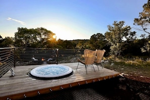 Eine Holzterrasse mit Whirlpool und Korbstühlen, mit Blick auf eine natürliche Landschaft mit Bäumen und einem Gewässer.