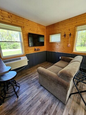 A room with wooden walls, a sofa, a TV, and a table with a chair.