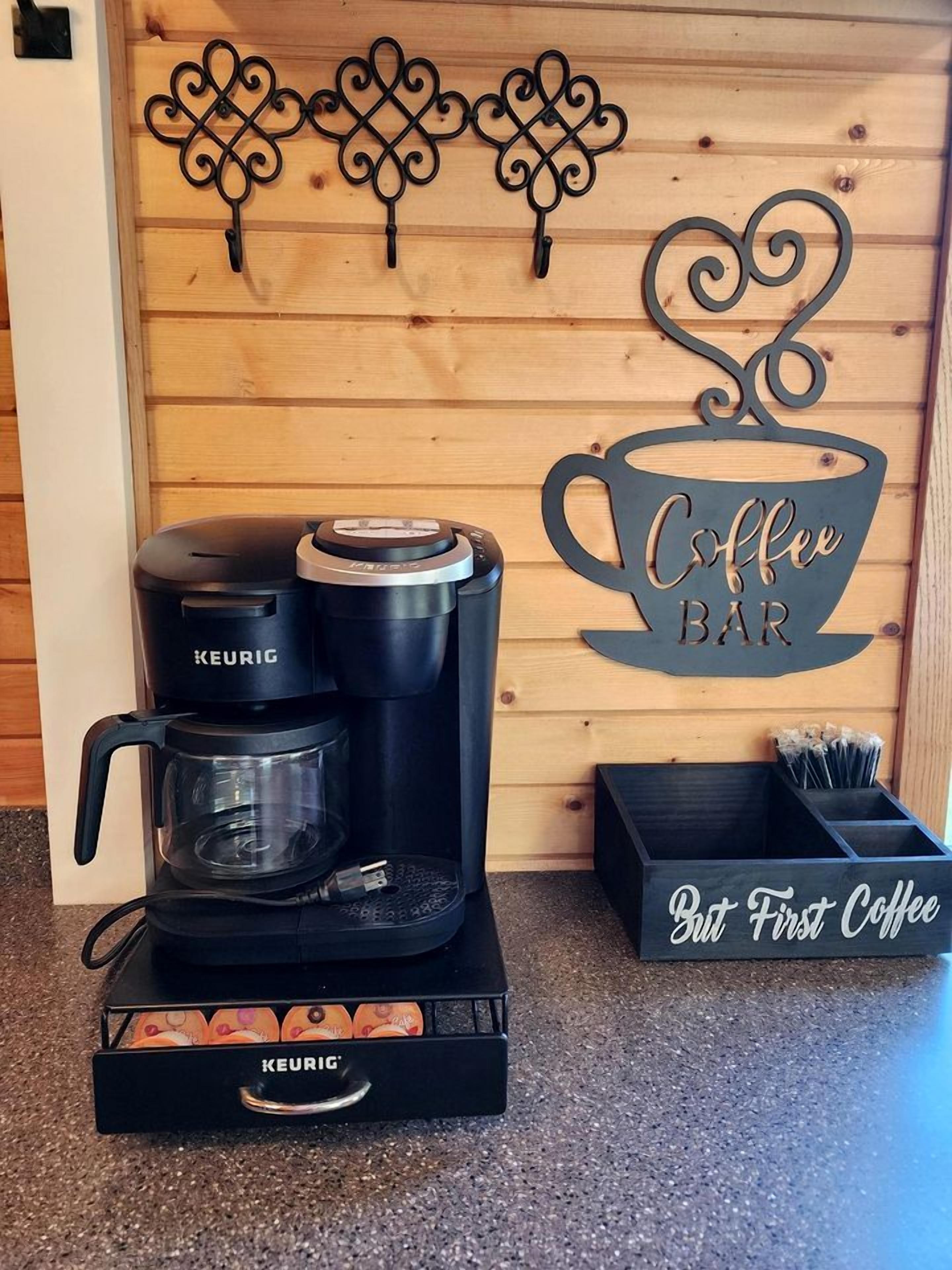 A coffee maker with a KEURIG logo, a coffee cup sign, and a box labeled 'But First Coffee'.