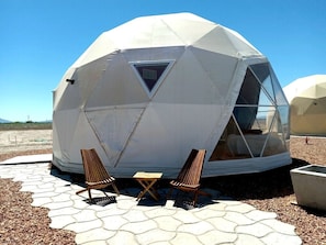 A geodesic dome structure with a triangular window, two wooden chairs, and a small table outside. - Impressive Dome with Great Panoramic Desert Views in Willcox, Arizona (Wilcox)