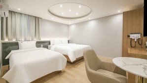 A hotel room with two beds, a desk, a chair, and a ceiling light fixture. - Hey Jecheon Hotel (Jecheon)
