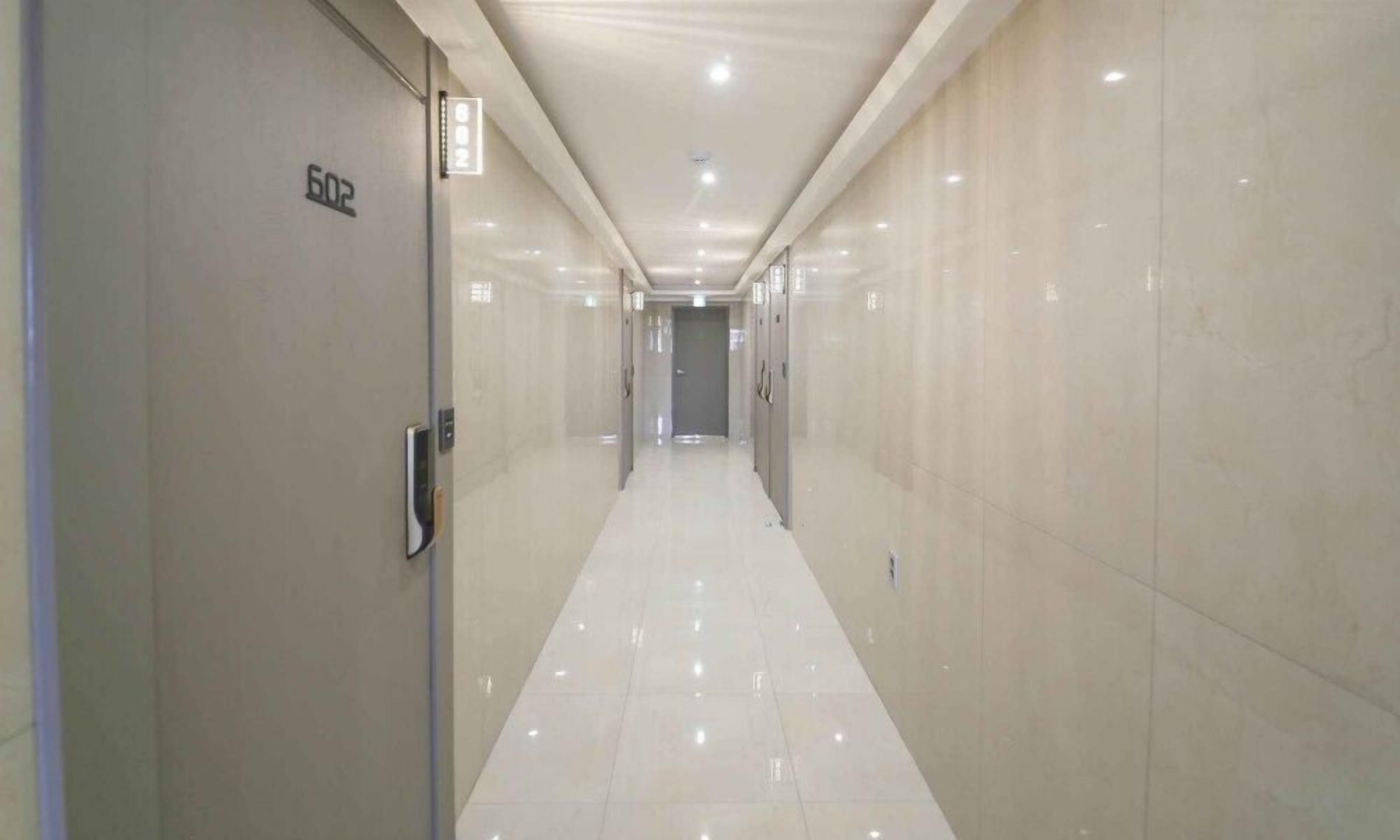 A long, narrow hallway with a tiled floor and walls, leading to a door at the end.