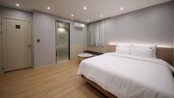 A hotel room with a large bed, a small round table, a wardrobe, and an air conditioning unit.