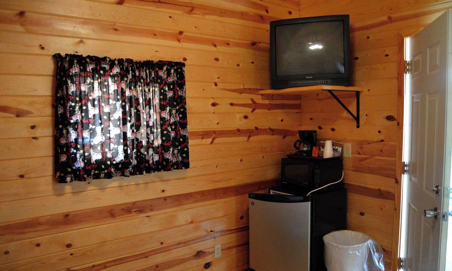 Ein kleines Zimmer mit Holzwänden, einem an der Wand befestigten Fernseher, einer Mikrowelle und einem Kühlschrank.