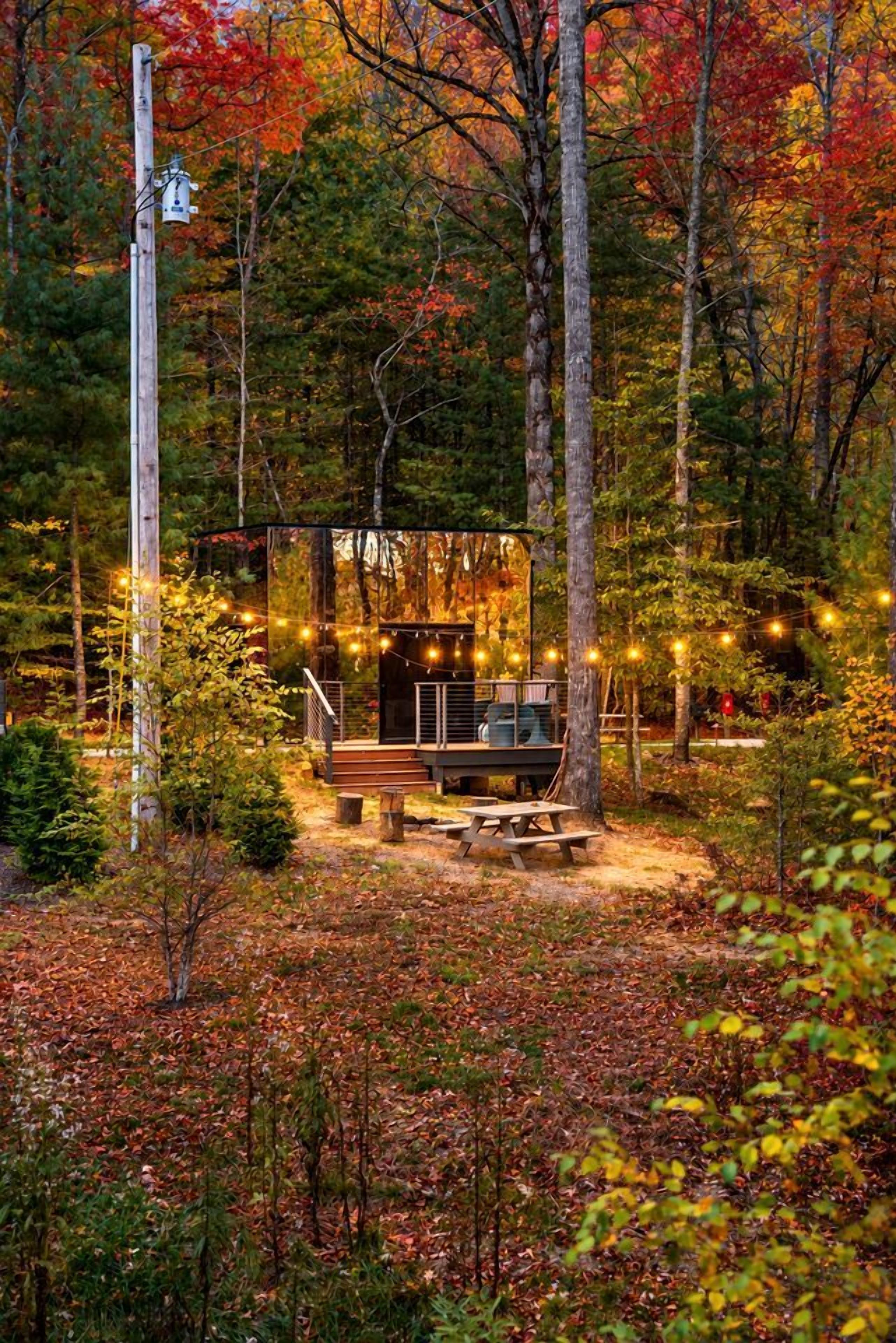 A cabin with a deck, surrounded by trees and a picnic table.