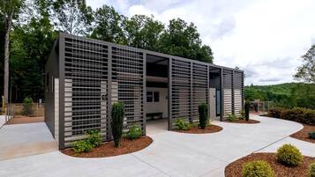 A modern building with a covered outdoor area, surrounded by landscaped gardens and trees.