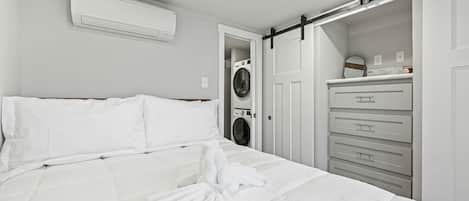 Quarto de hotel com cama, ar condicionado branco, máquina de lavar e porta de armário deslizante.