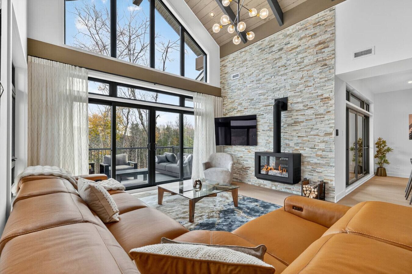 Ein modernes Wohnzimmer mit einer Steinwand, Ledersofas, einem Glastisch und einem Kamin.