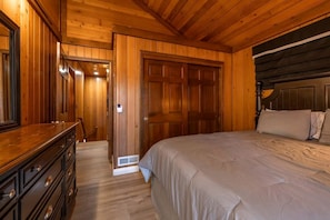 A wooden-paneled bedroom with a bed, dresser, and a door leading to another room. - Wonderful Cabin Nestled Amidst Trees with Foosball and Hot-tub in Big Bear Lake, California (Big Bear Lake)