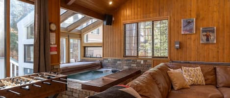 A cozy room with a wooden interior, a hot tub, a foosball table, and a leather couch.