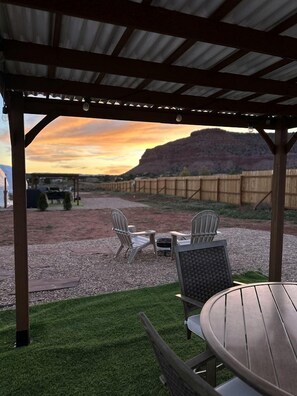 A covered patio with outdoor furniture, a view of a hilly landscape, and a gravel path.