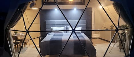 A geodesic dome room with a bed, bedside table, and a small seating area.