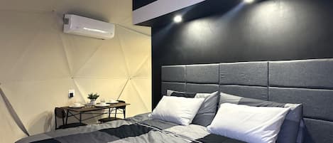 Een moderne slaapkamer met een groot bed, een klein tafeltje met een lamp en een wandairconditioner.