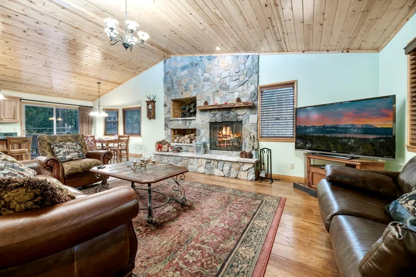 A spacious living room with a stone fireplace, leather sofas, a large flat-screen TV, and a view of the outdoors.