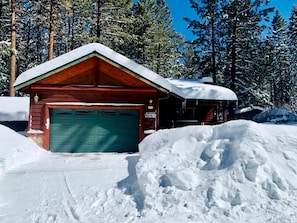 A wooden cabin with a green garage door, surrounded by snow and trees. - Comfy Cabin with Outdoor Living Space with Spa in Big Bear Lake (Big Bear Lake)