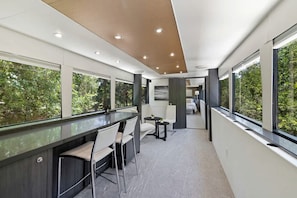 Ein modernes Interieur mit Barbereich, Sitzgelegenheiten und großen Fenstern mit Blick auf Grünflächen.