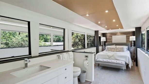 Une salle de bain moderne dotée d’un grand lavabo, de toilettes et d’un bidet, ainsi qu’une chambre séparée avec un lit et des tables de chevet.
