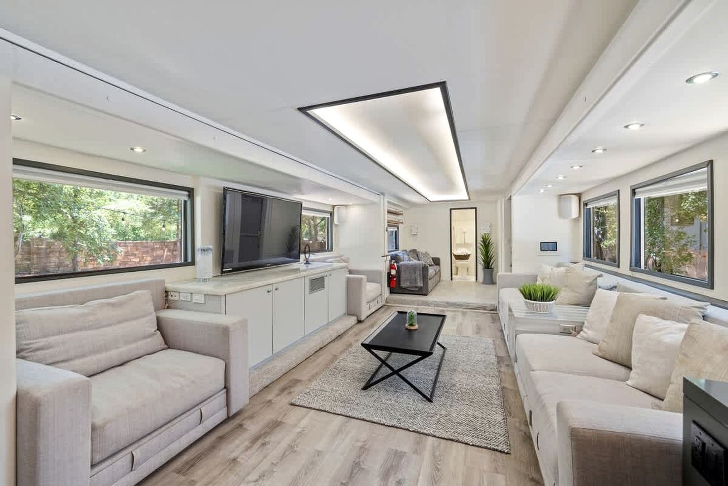 A spacious living area with a large TV, sofas, a coffee table, and a kitchen area.